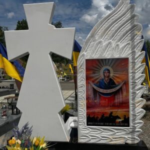 Обратная сторона белого памятника военному с резным крылом ангела, казацким крестом и иконой Покрова Пресвятой Богородицы.