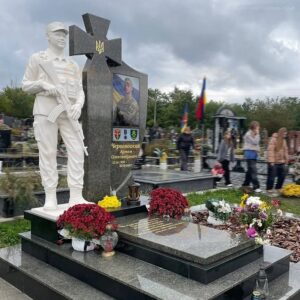 Общий вид установленного военного мемориала с казацким крестом, белой скульптурой воина и гранитной надгробной плитой на кладбище.